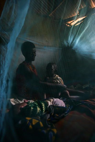 Una mujer africana y sus hijos, bajo un mosquitero contra la malaria tratados con insecticida.
