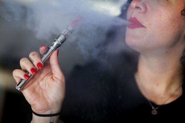 Una mujer que usa un e-cigarrillo, soplando el vapor que contiene nicotina.