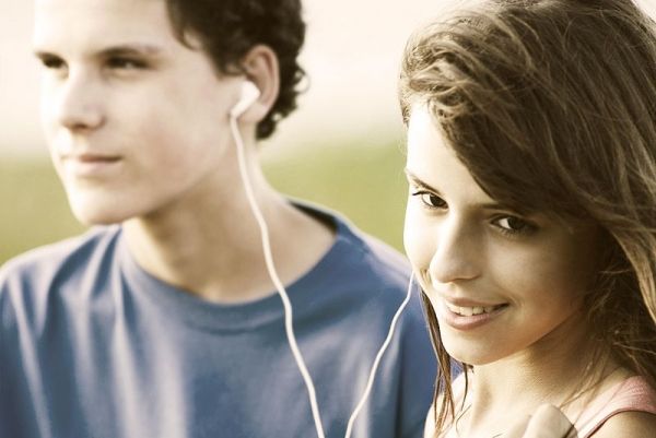 Adolescentes compartiendo auriculares, escuchando música al aire libre. El horario de verano.